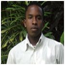 A young man in a white shirt standing in front of plants.