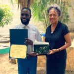 Two people holding certificates and a framed photo.